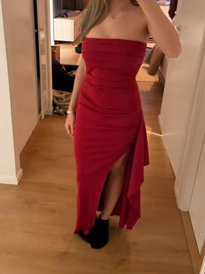 Vinröd axelbandslös långklänning - Elegant vinröd axelbandslös långklänning med draperad design. Perfekt för en festlig kväll eller bal.