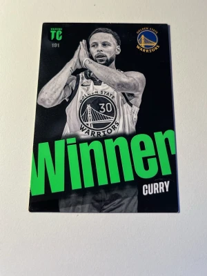 Rare Basketkort Golden State Warriors Curry - Säljer ett basketkort med motiv av Golden State Warriors och texten 'Winner' i grönt. Kortet har svartvit design med lagets logga och Curry på framsidan. Perfekt för samlare av sportkort eller NBA-merch.