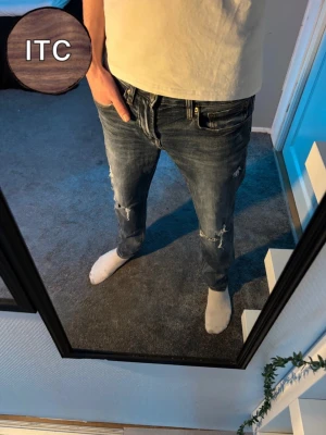 Jeans med slitningar  - Säljer ett par mörkblå skinny jeans från American Eagle med slitna detaljer och snygga rippade partier på benen. Jeansen har klassisk femficksdesign, låg midja och är tillverkade i mjukt bomullsmaterial med stretch för skön passform.