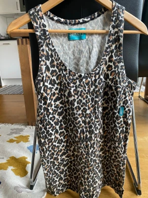 Leopardmönstrat linne från Junkyard - Snyggt linne från Junkyard med leopardmönster i svart, brunt och beige. Modellen har rund halsringning och en liten bröstficka med blå logotagg. Perfekt för dig som vill sticka ut med ett djurmönstrat plagg.