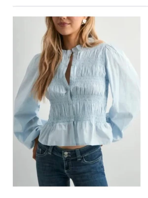 Ljusblå blus med puffärmar - Trendig ljusblå blus med smockdetaljer och volang nedtill. Blusen har hög krage, knäppning framtill och långa puffärmar💕heeelt oanvänd
