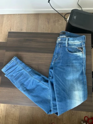 Blå jeans Replay - Säljer ett par blå slim fit jeans från Replay med snygga slitningar och klassisk femficksdesign. W28 L32. Jeansen har en ljus tvätt framtill och bakficka med Replay-logga på läderpatch. Perfekta för en avslappnad och trendig look.