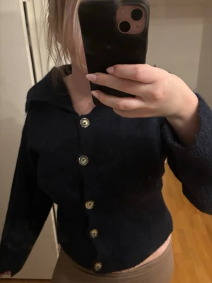 Mörkblå kofta med stora knappar - Säljer en mörkblå kofta med stora, silvriga knappar framtill. Koftan har en bred krage och långa ärmar. Materialet ser ut att vara mjukt och stickat, perfekt för lager på lager. Passar dig som gillar en enkel men snygg stil. Mer som en M!!💕💕