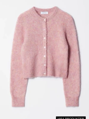 Rosa fluffig kofta från & Other Stories - Supersöt rosa kofta från & Other Stories i fluffigt material (ull och alpackablsndning) Kortare modell med rund halsringning och ton-i-ton färgade knappar framtill. Långa ärmar och ribbade muddar ger en mysig och trendig look. Perfekt att styla över en topp eller klänning.