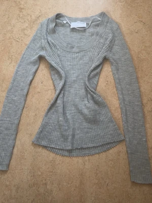 Grå ribbad topp från Selected Femme - Säljer en grå ribbad långärmad topp från Selected Femme. Toppen har en figurnära passform med markerad midja och rund halsringning. Tillverkad i mjukt material som känns skönt mot huden. Perfekt för att lyfta din vardagsstil. Endast provad 