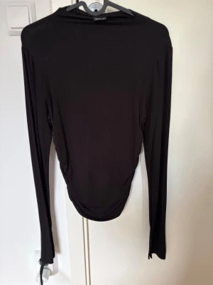 Svart långärmad topp från Gina Tricot - En enkel och stilren svart långärmad topp från Gina Tricot. Toppen har en tight passform och är tillverkad i ett mjukt, stretchigt material som känns skönt mot huden. Perfekt att styla med jeans eller kjol för en clean look. Finns inte längre tillgänglig i butik och online!