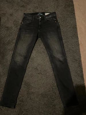 Svarta slim fit jeans från Replay - Snygga svarta slim fit jeans från Replay, modell Anbass. Jeansen har fem fickor, diskreta slitningar och klassisk knappgylf. Materialet är stretchigt denim som sitter tajt och bekvämt. Perfekta för en trendig och avslappnad look.