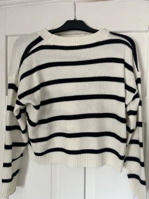Randig stickad tröja från SHEIN - Säljer en vit stickad tröja från SHEIN med svarta horisontella ränder. Tröjan har rund halsringning, långa ärmar och ribbade muddar vid ärmslut och nederkant. Perfekt för en avslappnad och trendig look.