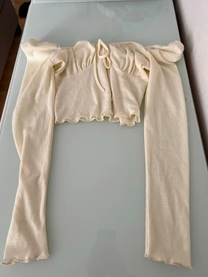 Ljusgul croppad topp med knyt - Trendig ljusgul croppad topp med långa ärmar och knyt framtill. Toppen har en ribbad struktur och volangkant nedtill för en söt touch. Perfekt för dig som vill ha en stilren men ändå lekfull look.