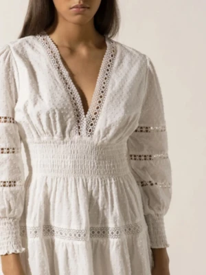 By Malina klänning strl S - Supersöt vit kortklänning med v-ringning och spetsdetaljer längs urringning, ärmar och kjol. Klänningen har lång ärm med smock vid ärmslut och markerad midja. Tillverkad i luftig bomull, perfekt för sommarens alla tillfällen. Fint skick. Nypris 2600 kr