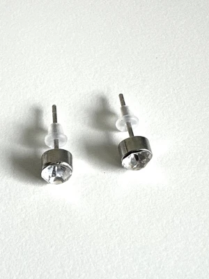 Silvriga örhängen med klar sten, helt NYA - Snygga örhängen i silverfärgad metall med rund, klar sten framtill. Klassisk och stilren design med stift och transparenta bakstycken. Perfekta för dig som gillar minimalistiska smycken med lite extra bling.