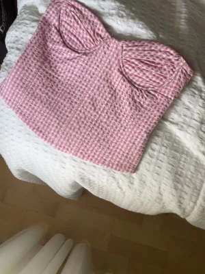 Rutig rosa korsettopp från Zara - Supersöt korsettopp från Zara i rosa och vitt rutigt mönster. Toppen är axelbandslös och har markerade kupor för en snygg siluett. Stängs med hyskor bak.