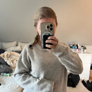 Ljusgrå oversized stickad tröja - Mysig ljusgrå stickad tröja med avslappnad, oversized passform och rund halsringning. Tröjan har långa ärmar och ribbade muddar vid ärmslut och nederkant. Perfekt för lager på lager och chill vardagsstil.