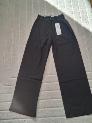 Svarta mjukisbyxor från Alo Yoga - Säljer ett par svarta mjukisbyxor från Alo Yoga med breda ben och elastisk midja. Byxorna har minimalistisk design med diskret logga både fram och bak. Perfekta för chill eller träning, tillverkade i mjukt och följsamt material.