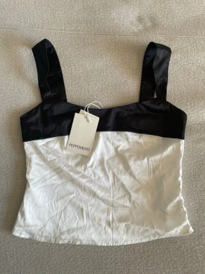 Svartvit satintopp från Peppermayo - Svartvit satin topp från Peppermayo med breda axelband. Toppen har en svart överdel och vit nederdel, vilket ger en stilren kontrast. Tillverkad i ett glansigt material som känns lyxigt och passar perfekt till många olika looks🤍🖤