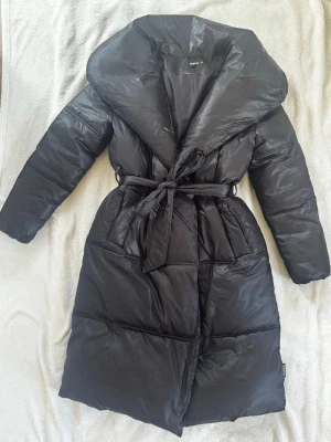 Missguided lång jacka med krage  - Lång jacka med krage från Missguided i storlek 38. Kedja halvvägs upp med band runt midjan. 