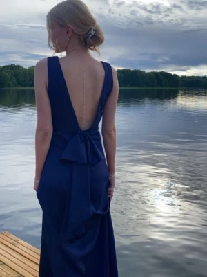 Marinblå balklänning - Elegant marinblå långklänning med djup öppen rygg och stor rosettdetalj baktill i midjan. Klänningen är stilren och figurnära. Perfekt för er som har bal snart!💕använd en gång🩷
