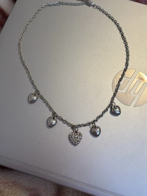 Silverfärgat halsband med hjärtberlocker - Ett silverfärgat halsband med fem hjärtformade berlocker, varav den i mitten är dekorerad med gnistrande gems. Kedjan är tunn och elegant, perfekt för att ge en söt touch till din outfit. Materialet är metall och designen är ungdomlig och trendig. Anledningen till att jag säljer den är pga att jag använder mig av guld, inte silver. Den va väldigt vacker😞 kommer tyvärr inte ihåg vart jag köpte den ifrån.