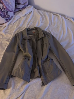 Grå skinnjacka från Only - Säljer på grund av inte min stil. Snygg grå skinnjacka från Only med klassisk krage, dragkedja framtill och två stora fickor. Jackan har justerbara spännen i midjan och markerad midjeskärning för en schysst siluett. Perfekt för dig som gillar stilrena och tidlösa plagg.