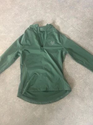 Grön långärmad träningströja - Snygg grön långärmad träningströja från ICANIWILL med halv dragkedja framtill och en vit geometrisk logga på bröstet. Tillverkad i ett stretchigt funktionsmaterial som passar perfekt till träning och aktiva dagar bra sick 