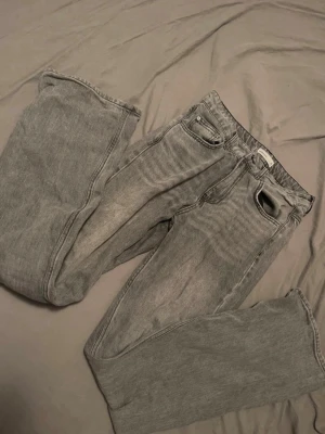 Grå bootcut jeans med vintagekänsla - Säljer ett par grå jeans med bootcut och klassisk femficksdesign. Jeansen har en tvättad look som ger en snygg vintagekänsla och är tillverkade i denim. Perfekta för dig som gillar en avslappnad och stilren stil.