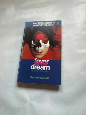 Fever Dream & Other Fantasies - En pocketbok med titeln 'Fever Dream & Other Fantasies' av Ray Bradbury och Robert Bloch. Omslaget är blått och rött med konstnärlig illustration. Boken innehåller flera science fiction- och skräcknoveller. Perfekt för dig som gillar mörka och mystiska berättelser.