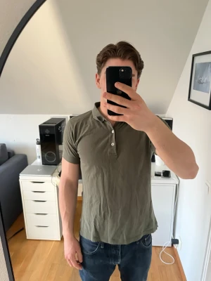 Olivgrön pikétröja från Oscar Jacobson - Säljer en stilren olivgrön pikétröja från Oscar Jacobson . Tröjan har klassisk krage, tre vita knappar framtill och korta ärmar. Hör gärna av dig vid frågor!