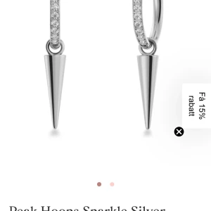 Edblad peaks hoops sparkle silver - Snygga hoops i silverfärg med gnistrande stenar längs hela ringen och en spetsig, konformad hängande detalj. Örhängena har en modern och edgy look som sticker ut. Perfekta för dig som gillar statement-smycken och vill addera lite extra bling till din stil.