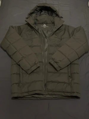 Navy green dunjacka  Whistler - Säljer en svart dunjacka oanvänd från Whistler i storlek M. Jackan har en praktisk huva, dragkedja framtill och två sidofickor med dragkedja. Puffig design med horisontella sömmar och elastiska muddar vid ärmsluten. Perfekt för kalla vinterdagar.