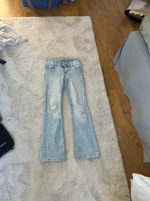 Ljusblå bootcut jeans - Säljer ett par ljusblå bootcut jeans med klassisk femficksdesign och låg midja. Jeansen har slitna detaljer framtill och är tillverkade i ett mjukt denimtyg. Perfekta för en avslappnad och trendig look.