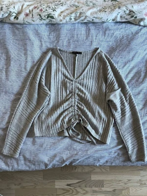 Ljusgrå  ribbad stickad tröja med knyt - En ljusgrå långärmad ribbad tröja med knyt som går att justera.