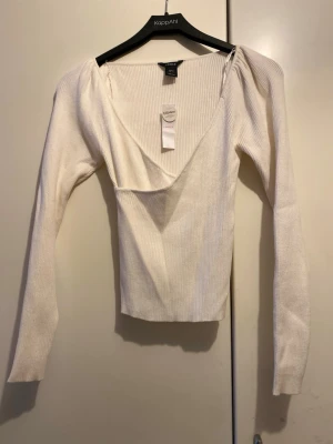 Vit ribbad topp från Lindex - Trendig vit ribbad topp från Lindex med djup v-ringning och långa ärmar. Tillverkad i ett mjukt material med EcoVero-viskos som känns skönt mot huden. Perfekt för dig som gillar stilrena och enkla plagg med en twist.