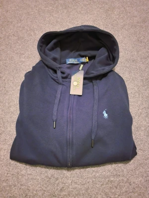 Ralph Lauren zip up/kofta - Snygg mörkblå hoodie från Polo Ralph Lauren med dragkedja och huva med snörning. Den är I storlek M kan även passa S. Tillverkad i 100% mjuk bomull. OBS: färgen ser lite dåligare ut på bilden men inte i verkligheten. Vid snabbaffär kan priset diskuteras och även frakta vid det första tillfället.