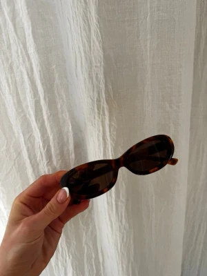 Ovala solglasögon i leopardmönster - Snygga ovala solglasögon med leopardmönstrad båge i bruna toner. Glasen är mörka och bågarna har en retroinspirerad form som ger en cool vibe. Perfekta för att lyfta vilken outfit som helst.