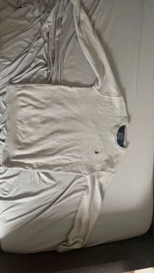 Ljusgrå stickad tröja Polo Ralph Lauren - Säljer en stilren ljusgrå stickad tröja från Polo Ralph Lauren med den klassiska mörkblå loggan broderad på bröstet. Tröjan har rund halsringning och långa ärmar, perfekt för lager på lager och enkel att matcha till olika outfits.