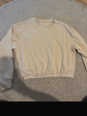 Beige sweatshirt i storlek XS/S - En basic beige sweatshirt med rund halsringning och ribbade muddar vid ärmslut och nederkant. Tröjan har en avslappnad passform och är tillverkad i mjukt bomullsmaterial. Perfekt för en chill och enkel stil.