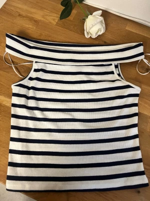 Randig offshoulder topp från H&M Divided - Säljer en vit och marinblå randig offshoulder topp från H&M Divided. Toppen är ribbad och har axelbandslös design med bred kant upptill. Perfekt för sommarens alla tillfällen!
