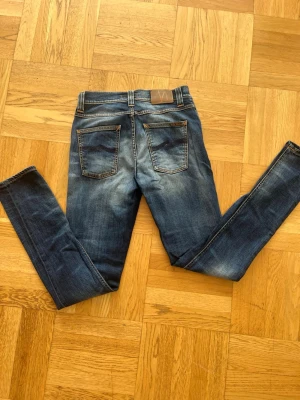 Nudie jeans - Snygga blå skinny jeans från Pull&Bear med slitningar och tvättade detaljer. Klassisk femficksmodell med normal midja och smala ben. Jeansen har kontrastsömmar och patch bak i midjan. Perfekta för en avslappnad och trendig look. Priset kan diskuteras vid snabb affär😎