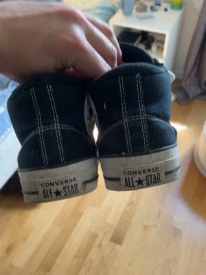 Svarta Converse All Star Highs - Klassiska svarta Converse All Star sneakers med vita gummisulor och tåhättor. Skorna har vita snören och tydliga kontrastsömmar. Märket syns både på plösen och hälen. Tillverkade i canvas med hög modell för en tidlös streetstil.