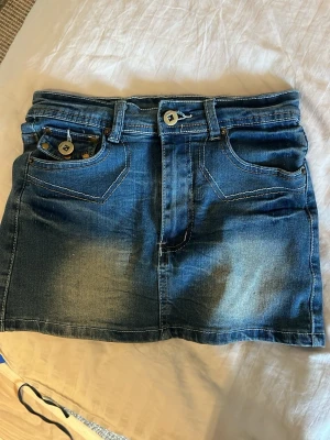 Knappt använd superfin jeanskjol - Jättefin kort jeanskjol i blå denim med slitningar och dekorativa nitar på fickorna. Kjolen kan användas till varma sommardagar men också när man vill känna sig extra fin💗 Perfekt för dig som gillar en avslappnad och trendig stil.