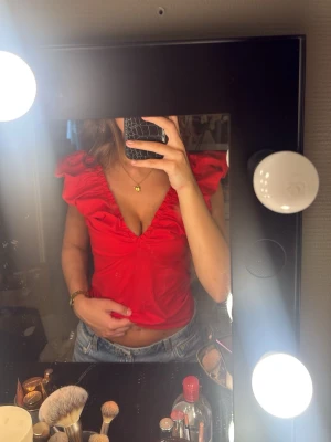 Röd volangtopp med v-ringning - Snygg röd topp med djup v-ringning och volangdetaljer längs axlarna. Modellen är croppad och har en figurnära passform. Perfekt att styla med jeans eller kjol för en trendig look. Använd fåtal gånger utan defekter, orgpris är 300💗