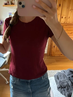 Mörkröd t-shirt i bomull - En enkel och stilren mörkröd t-shirt med rund halsringning. Tillverkad i mjuk bomull och har en normal passform med korta ärmar. Perfekt att matcha med jeans eller kjol för en avslappnad look.