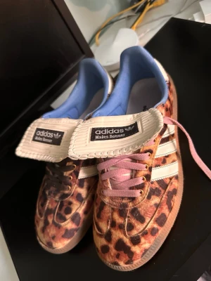 Adidas Wales Bonner leopard sneakers - Unika sneakers från Adidas och Wales Bonner med leopardmönstrad ovandel i päls, klassiska vita stripes och gummisula. Ena skon har bruna skosnören och den andra rosa, samt blått innerfoder och extra lång plös med branding. Perfekt för dig som vill sticka ut. Skorna är fåtal gånger använda om i väldigt bra skick vilket sticker ut för sådana sällsynta skor! Verkligen något att lägga på hyllan i samlingen eller styla till någon fet outfit🔥