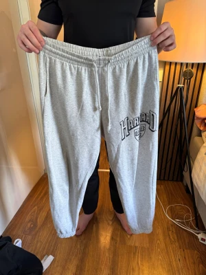 Grå Harvard mjukisbyxor med tryck - Säljer ett par grå mjukisbyxor från Harvard med tryck på ena benet. Byxorna har resår i midjan med dragsko och muddar vid bensluten. Perfekta för chill dagar hemma eller till träningen. Klassisk college-stil och mjukt material.