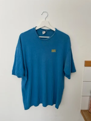 Blå oversized t-shirt - Blå oversized t-shirt med gul text 'SMILE' på bröstet från Junkyard i storlek M. Skriv vid intresse!
