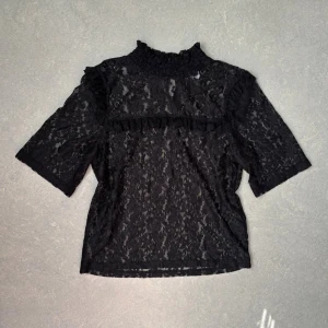 Svart spetsblus med volangdetaljer - Svart spetsblus med hög krage och volangdetaljer över bröstet. Från H&M i storlek 32. Blusen är see-through (se bilder)!❤️