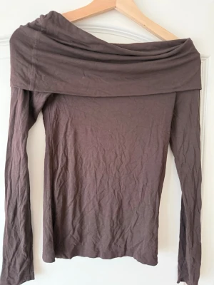 Brun offshoulder topp från Kappahl - Snygg brun offshoulder topp från Kappahl i mjukt material. Långärmad modell med bred krage som kan bäras nedanför axlarna för en trendig look. Perfekt att styla med jeans eller kjol för en cool outfit.