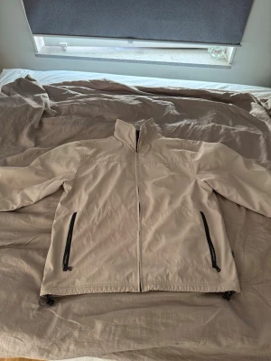 Beige vindjacka med svarta detaljer - Stilren beige vindjacka med hög krage och svarta dragkedjor på fickorna. 