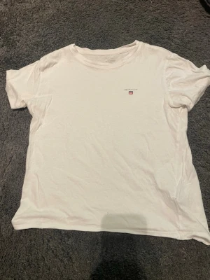 Vit t-shirt från Gant - Klassisk vit t-shirt från Gant med liten logga och sköld på bröstet. T-shirten har rund halsringning och korta ärmar. Perfekt basplagg i mjuk bomull som passar till allt.
