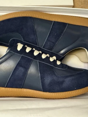 Maison Margiela gats - Snygga marinblå sneakers med ovandel i mocka och släta läderpaneler. Skorna har vita snören och en klassisk gummisula i brunt. Perfekt för dig som gillar stilrena och tidlösa sneakers med en sportig vibe.